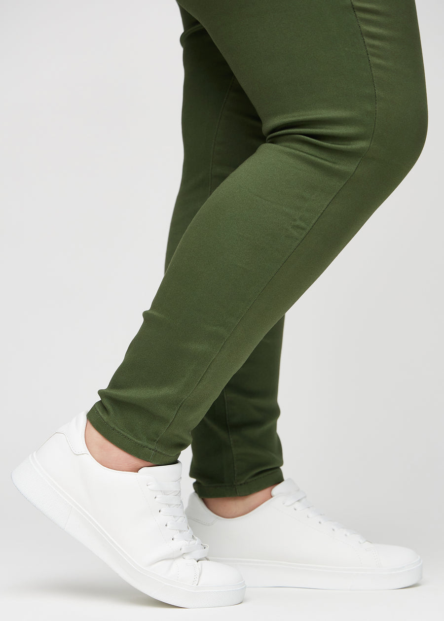 Skinny jeans for women in dark green, color Renewals. Close-up of the snug-fitting leg openings at the ankles on a plus-size model.