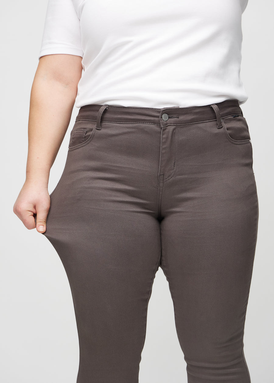 The plus-size model stretches the jeans at the thigh to show the stretch.