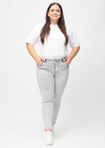 Full image of a plus-size model in light grey denim slim jeans.
