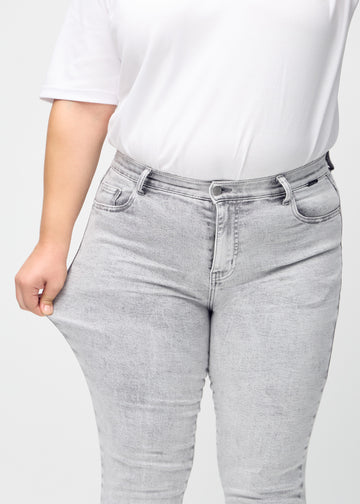 The plus-size model stretches the jeans at the thigh to show the stretch.