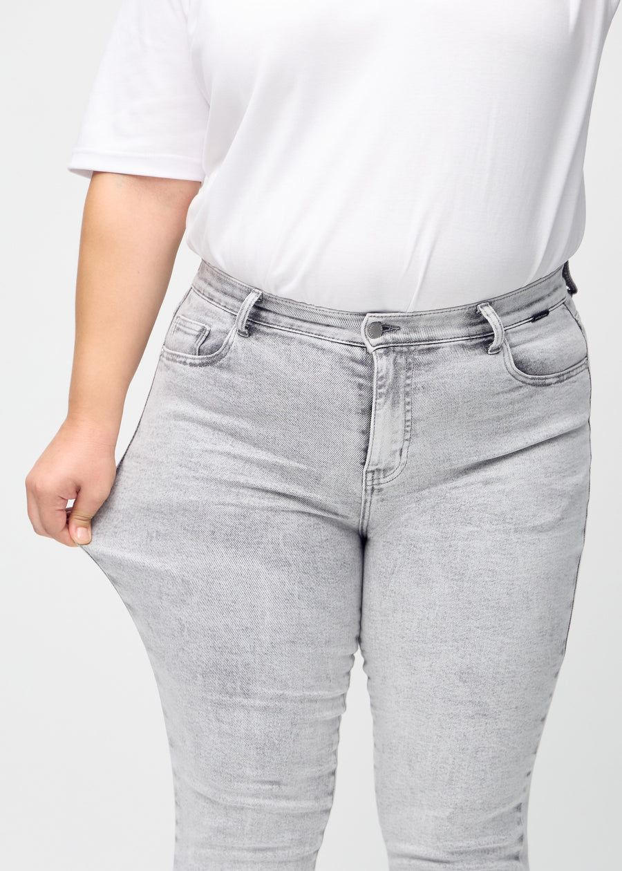 The plus-size model stretches the jeans at the thigh to show the stretch.