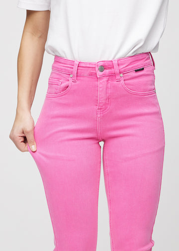 Slim jeans for women in light pink, color Flamingos. A model stretches the jeans at the thigh to show the fabric&