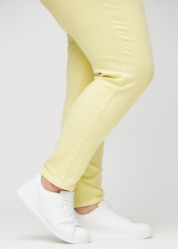 Slim jeans for women in light yellow, color Lemonades. Close-up at the ankles on a plus-size model, showing the fit at the leg openings.