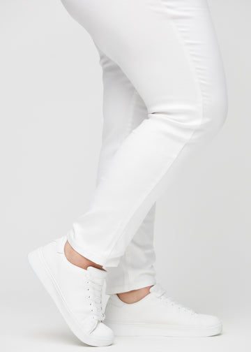 Slim jeans for women in white, color Marguerites. Close-up at the ankles on a plus-size model, showing the fit at the leg openings.