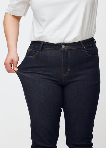The plus-size model stretches the deep dark blue denim jeans for women in the color Midnights at the thigh to show the material&