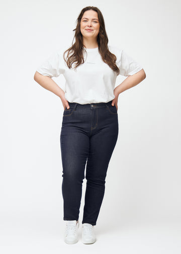 Full-length image of a plus-size model in deep dark blue denim jeans for women in the color Midnights with a slim fit.