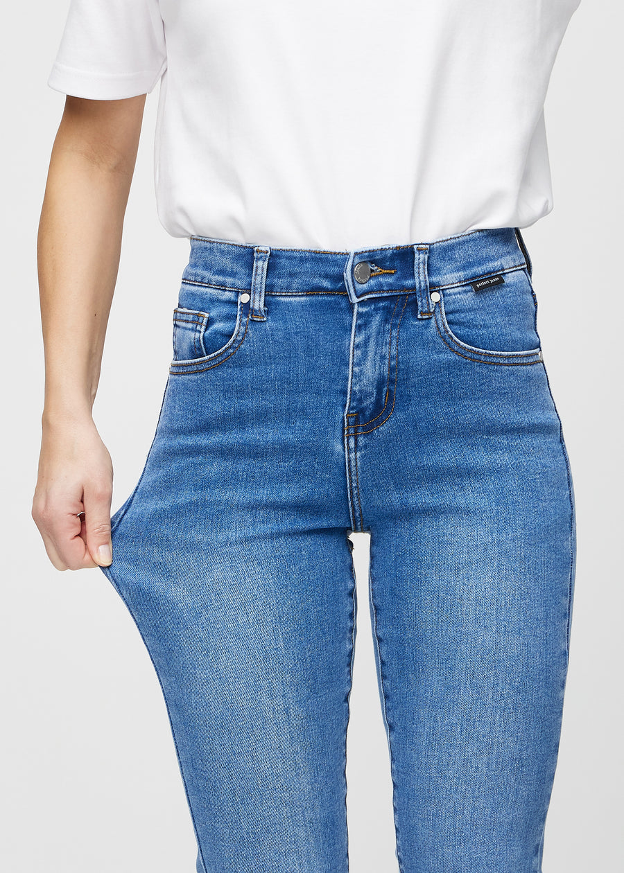 Slim jeans for women in blue, color Rivers. A model stretches the jeans at the thigh to show the fabric&