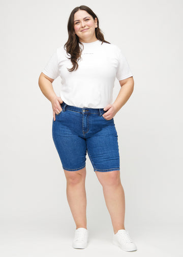 Full image of a plus-size model in dark denim skinny middle shorts.