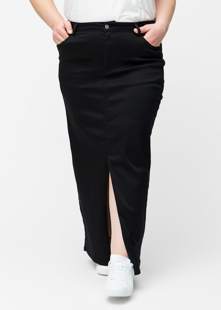 Lang, sort jeansnederdel i farven Ravens med regulær pasform set forfra på plus-size model, med slids foran der starter lige under knæet.