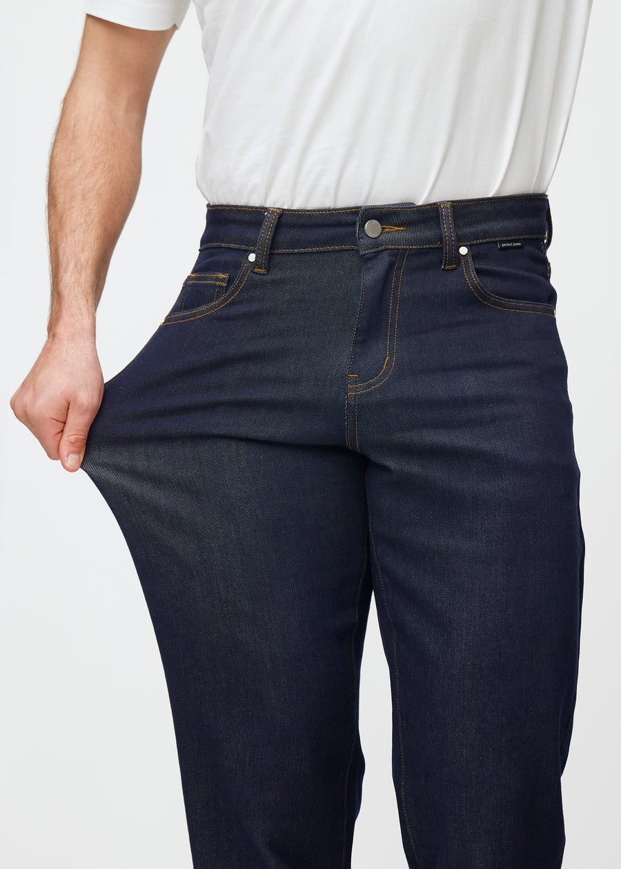 The model stretches the deep dark blue denim jeans for men in the color Midnights at the thigh to show the material&
