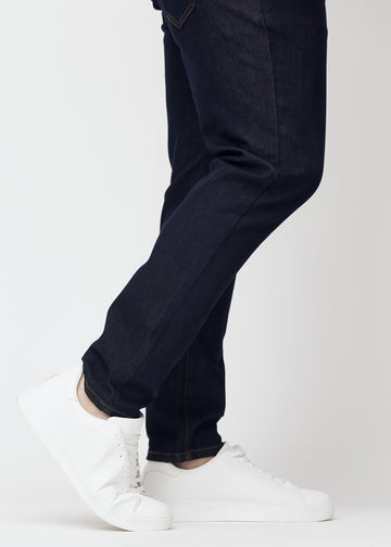 Deep dark blue denim jeans for men in the color Midnights with a slim fit seen close up at the ankles on a plus-size model to show the narrow finish.
