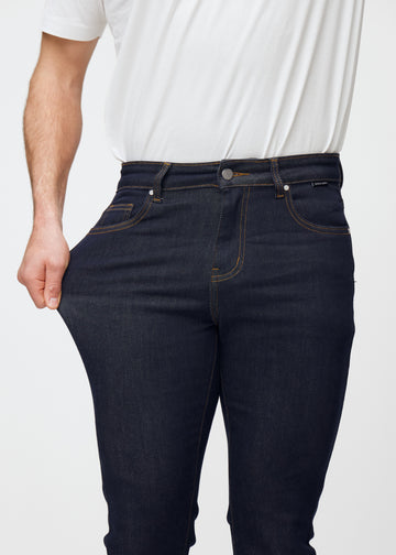 Model stretches deep dark blue denim jeans for men in the color Midnights at the thigh to show the material&