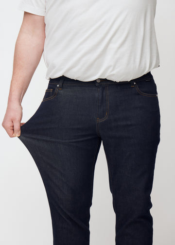 Plus-size model stretches deep dark blue denim jeans for men in the color Midnights at the thigh to show the material&