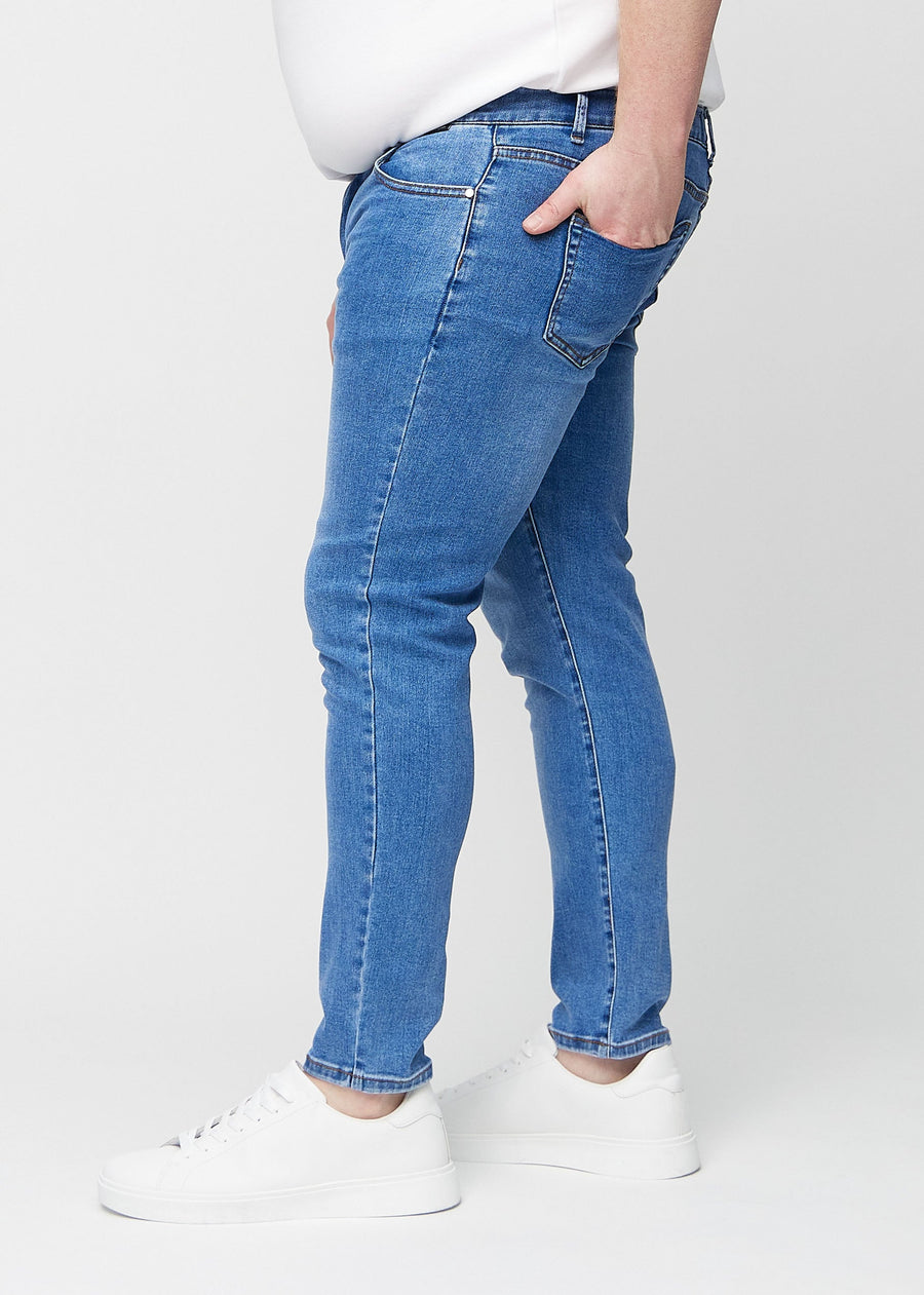 Blue denim slim jeans viewed from the side on a plus-size model.