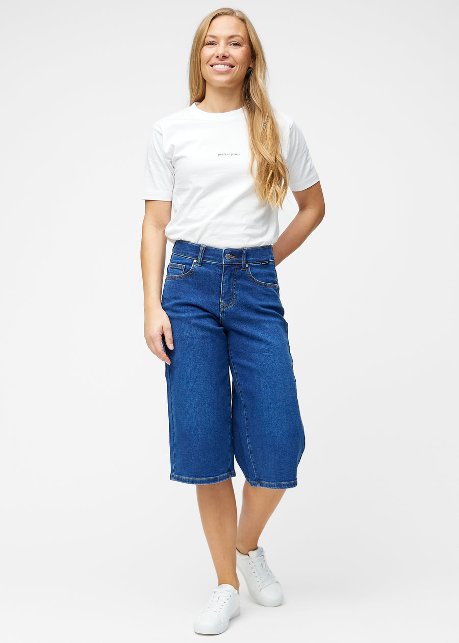 Model viser løse, mørkeblå denim capris i farven Oceans i bevægelse og demonstrerer pasform og materiale.