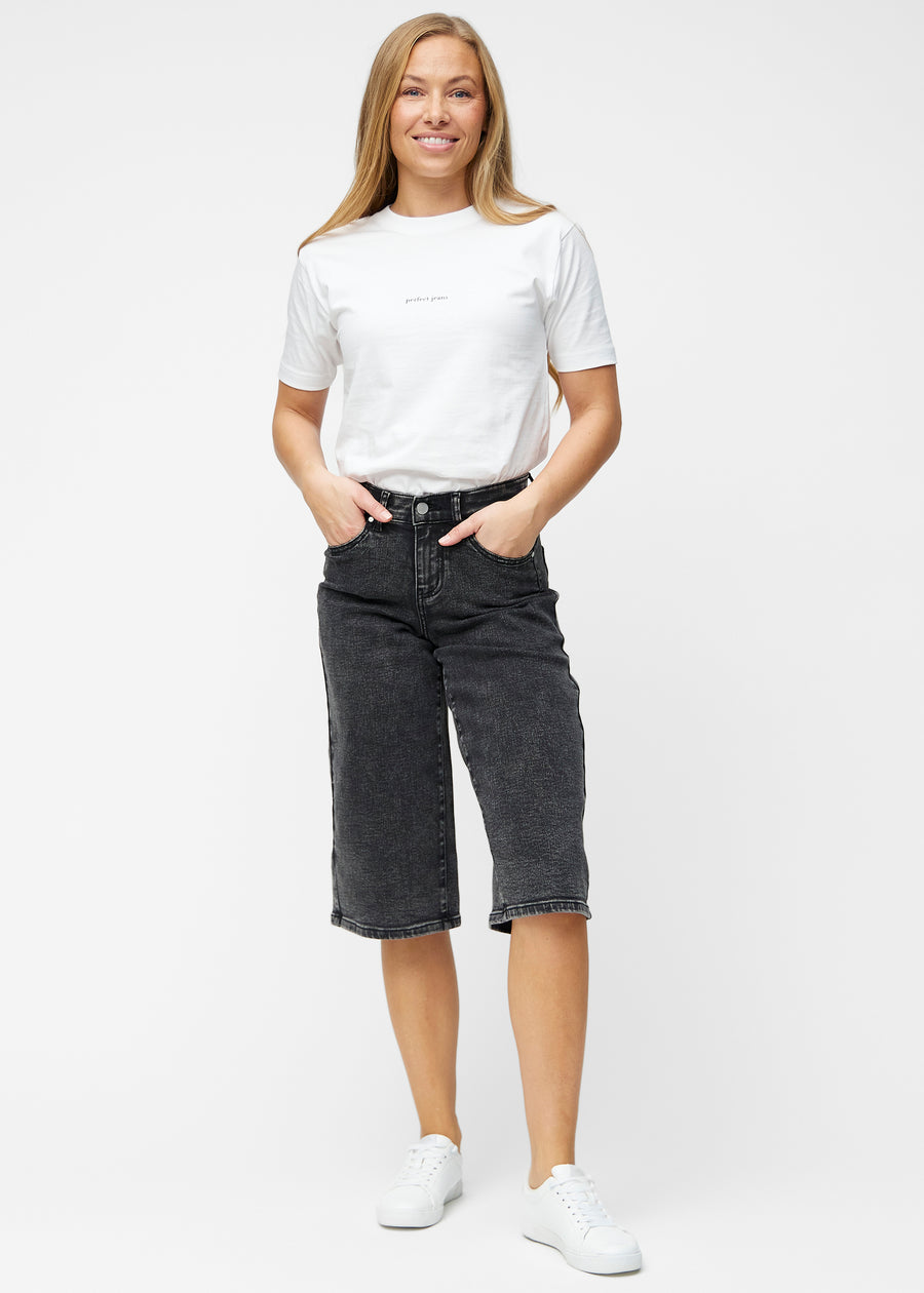 Model viser løse, mørkegrå denim capris i farven Shadows i bevægelse og demonstrerer pasform og materiale.