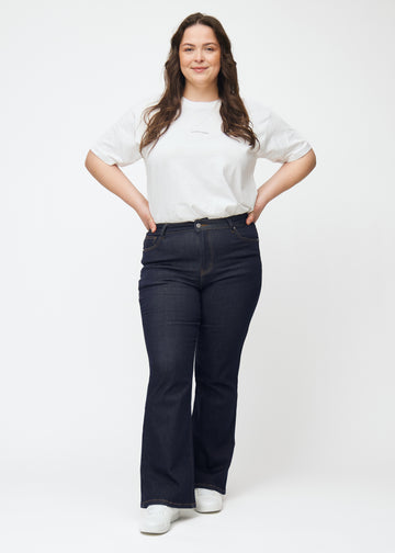 Plus-size model viser dyb mørkeblå denim jeans til kvinder i farven Midnights med bootcut pasform i bevægelse.
