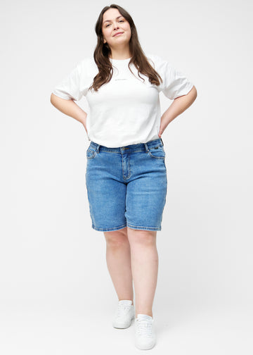 Plus-size model viser løse, klassisk blå denim shorts i farven Rivers i bevægelse og demonstrerer pasform og materiale.