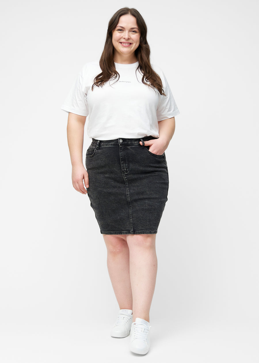 Plus-size model viser mørkegrå, tætsiddende og knælang denimnederdel i bevægelse og strækker materialet.